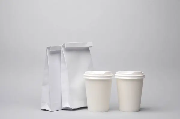 Paper lunch bags with cardboard coffee cups on gray background. Template for design mockup