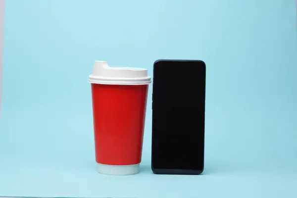 Disposable coffee cup with smartphone on blue background