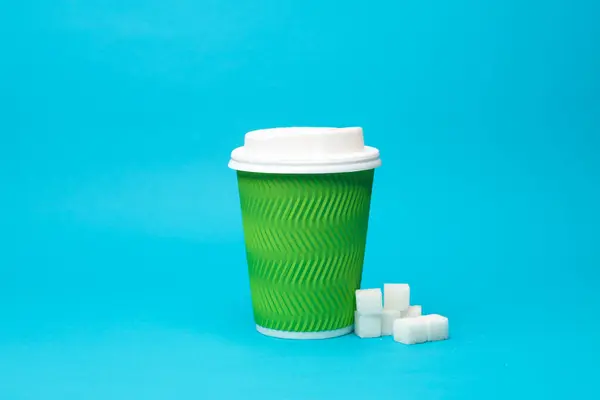 Disposable cardboard cup and sugar cubes on blue background