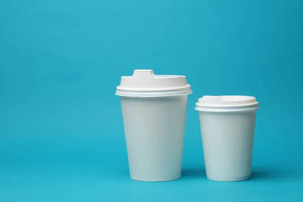 Mockup of white disposable cups with lids for hot drinks on a blue background