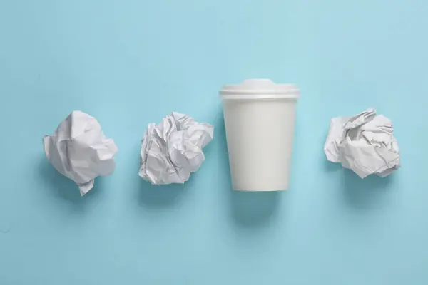 White disposable cup with crumpled paper balls on a blue background. Business concept photo