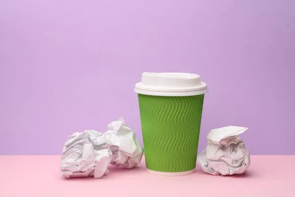 Disposable cup with crumpled paper balls on purple background. Business concept photo