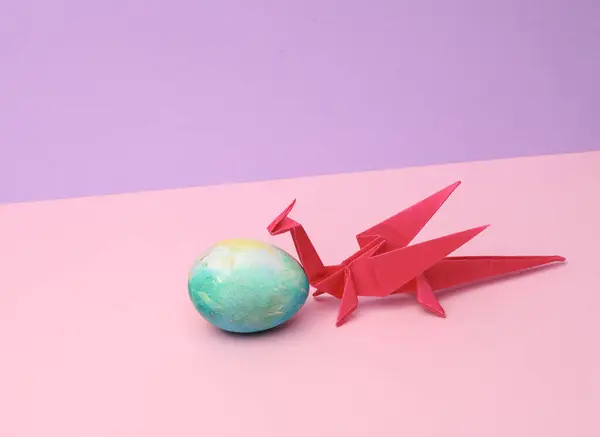 Origami dragon with colored egg on a pastel background. Conceptual easter photo