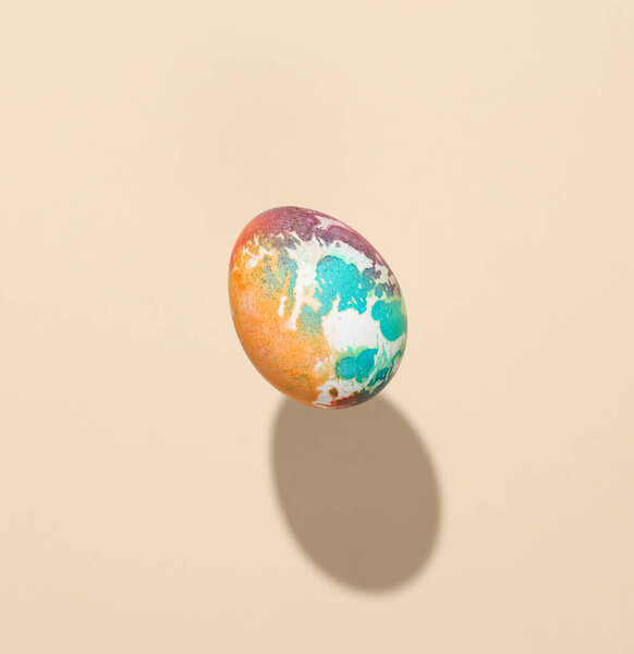 Multicolored Easter egg levitating on beige background with a shadow