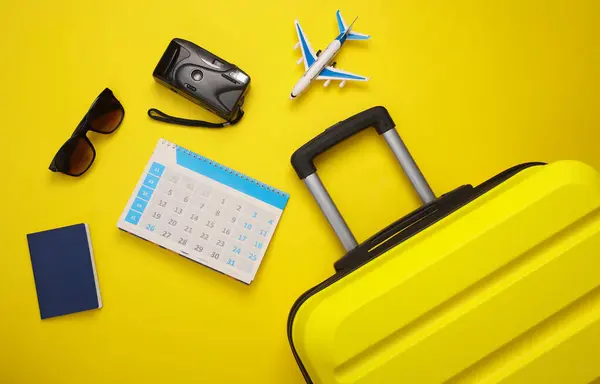 Vacation planning. Yellow Luggage suitcase with passport, calendar and travel accessories on a yellow background. Top view. Flat lay