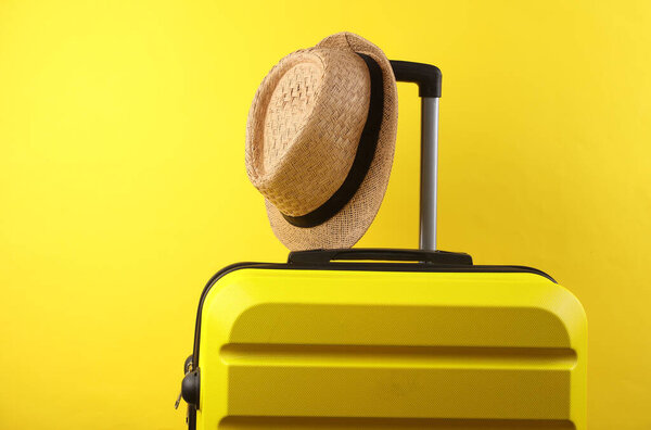Yellow plastic travel suitcase with hat on a yellow background. Luggage, tourism, vacation, relocation concept