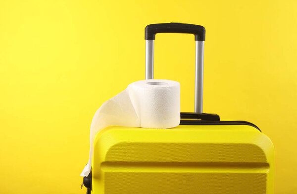 Yellow plastic travel suitcase and toilet paper roll on a yellow background. Tourism, vacation concept