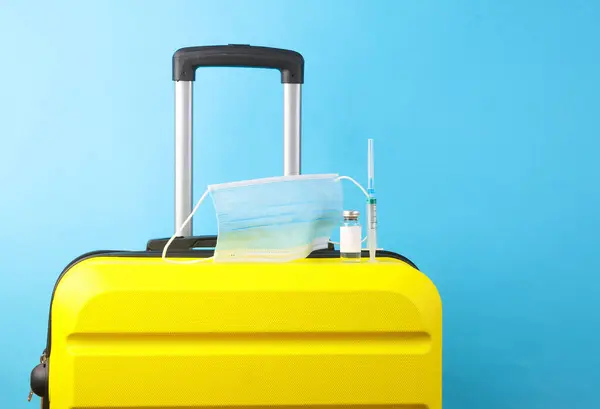 Travel suitcase with a medical mask and vaccine on blue background. Quarantine, covid 19, vaccination, travel rules