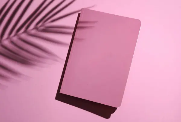 Pink notebook cover on pink pastel background with palm leaf shadow. Creative layout.