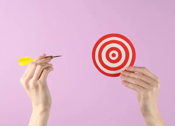 Hand holds darts and target on a purple background. Goal, business concept