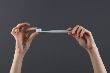 Koyu gri arka planda diş fırçası tutan eller. Diş bakımı, ağız temizliği konsepti