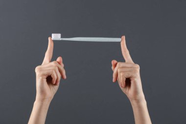 Koyu gri arka planda diş fırçası tutan eller. Diş bakımı, ağız temizliği konsepti