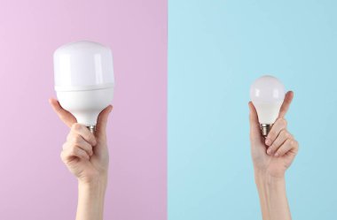 Kadın eli, mavi-pembe arka planda iki tane kurşun ampul tutuyor.