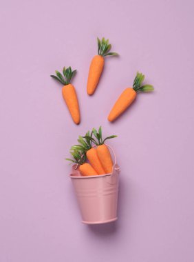 Pembe arka planda havuçlu minyatür kova.