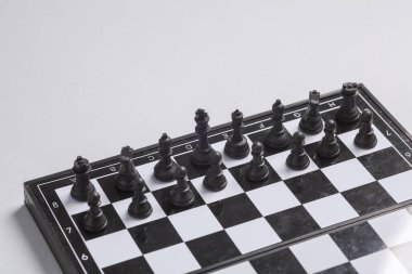 Beyaz arkaplanda siyah satranç taşları olan satranç tahtası.