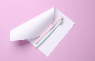 Eflatun arka planda, üzerinde kağıt olan diş fırçaları. Yaratıcı yerleşim