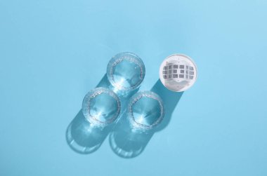 Su filtrelemek için kartuş filtresi ve gölgeli mavi zemin üzerinde temiz su bardakları. Sağlık Hizmetleri.