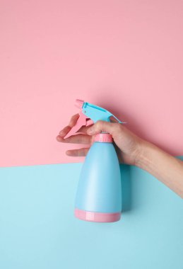 Mavi pastel arka planda, el ele tutuşan sprey şişesi.
