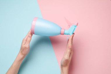 Mavi pastel arka planda sprey şişesi tutan eller.