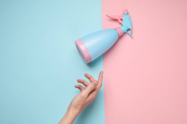 Mavi pastel arka planda, el ele tutuşan sprey şişesi.