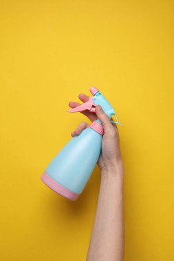 Sarı arka planda el ele tutuşan sprey şişesi