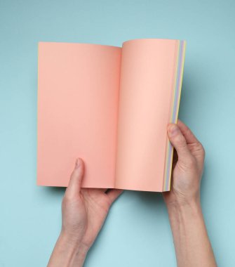 Kadın elleri mavi arkaplanda pembe boş sayfaları olan açık bir defter ya da dergi tutar