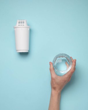 Mavi pastel arka planda suyu filtrelemek için bir bardak temiz su ve kartuş filtresi tutan eller. Sağlık Hizmetleri. Üst görünüm