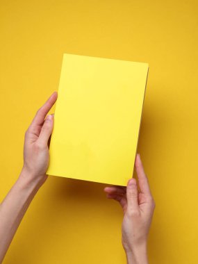 Sarı arka planda sarı kapaklı bir defter tutan eller