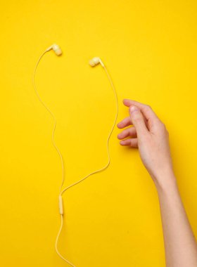 Sarı arka planda telli kulaklıklı bir el. Müzik aşığı