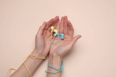 Kadın eli, bej arka planda mavi ve sarı kablolu kulaklıkları tutar.