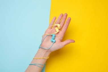 Mavi sarı arka planda mavi ve sarı kulaklıkları tutan kadın elleri var.