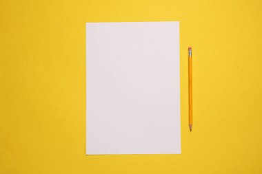 Sarı zemin üzerinde kurşun kalem olan beyaz boş bir kağıt.