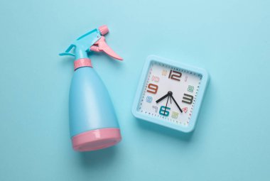 Mavi arka planda saati olan sprey şişesi