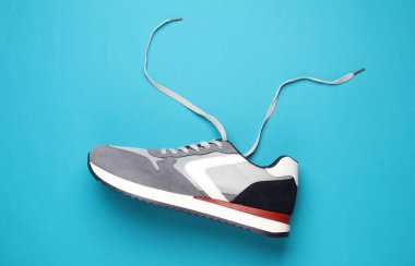 Mavi arka planda bağcıkları çözülmüş spor ayakkabı.