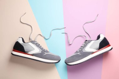 Pastel arka planda bağcıkları çözülmüş spor ayakkabılar. Üst görünüm