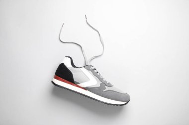 Gri arka planda bağcıkları çözülmüş spor ayakkabı.