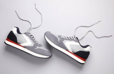 Gri arka planda bağcıkları çözülmüş spor ayakkabılar. Üst görünüm