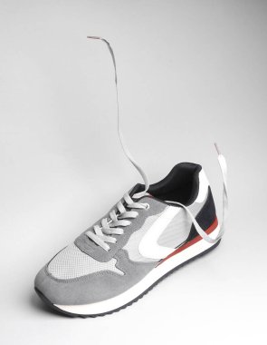 Gri arka planda yüzen bağcıklı gri spor ayakkabılar.