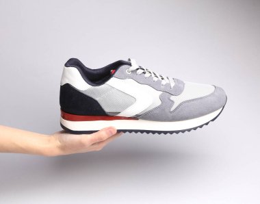 Gri arka planda gri spor ayakkabısı tutan