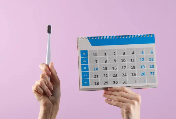 Hands hold toothbrushes and a calendar on a pastel background. Dental care, visit to the dentist