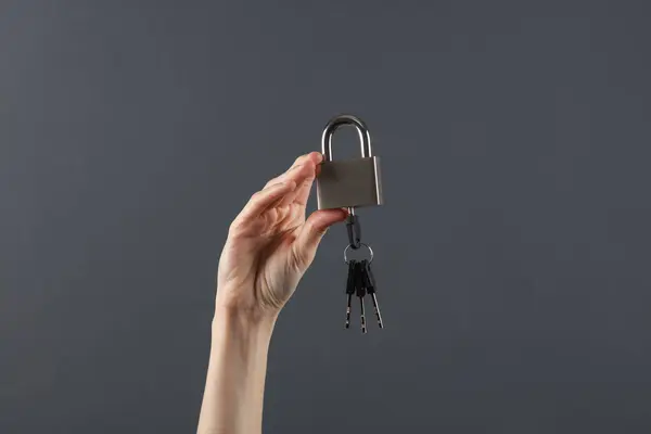 Hand holding lock with key on dark gray background