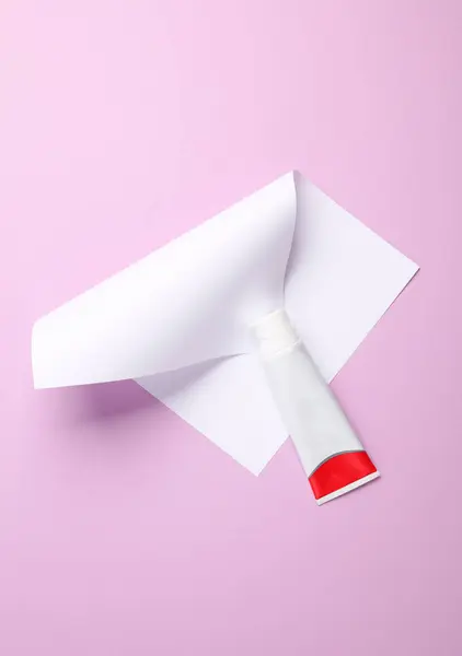 Toothpaste tube with a sheet of paper on a magenta background. Creative layout