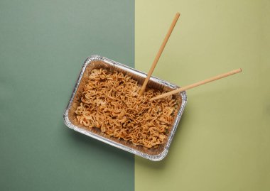 Yeşil arka planda yemek çubukları olan folyoda hazır şehriye. Üst görünüm