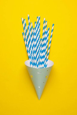 Sarı arka planda kokteyl tüpleri olan doğum günü konisi kapağı. Parti konsepti. Üst görünüm