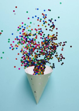 Mavi arka planda konfeti olan doğum günü konisi kapağı. Parti konsepti. Üst görünüm