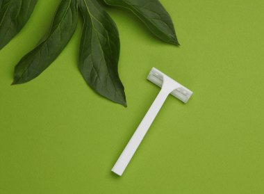 Yeşil arka planda yeşil yapraklı tek kullanımlık plastik jilet. Üst Manzara. Yaratıcı yerleşim