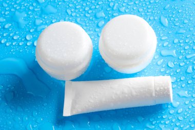 Beyaz krema tüpü ve mavi arka planda su damlaları olan kavanozlar. Güzellik konsepti