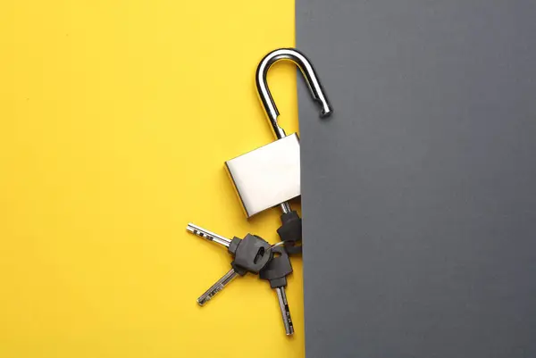 Opened metal lock with keys on yellow gray background
