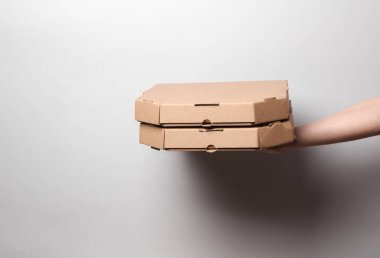 Gri arka planda gölgeli pizza kutularını tutan eller.