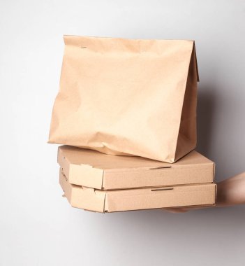 Paket yemek. Sıfır kayıp. El ele tutuşan mukavva pizza kutuları ve gri arka planda kağıt torba. Eko kavramı.